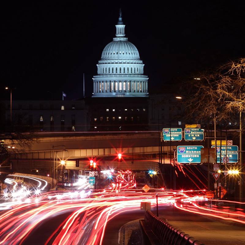 Nighttime view of the US Capitol building with a time-lapse of cars speeding by below