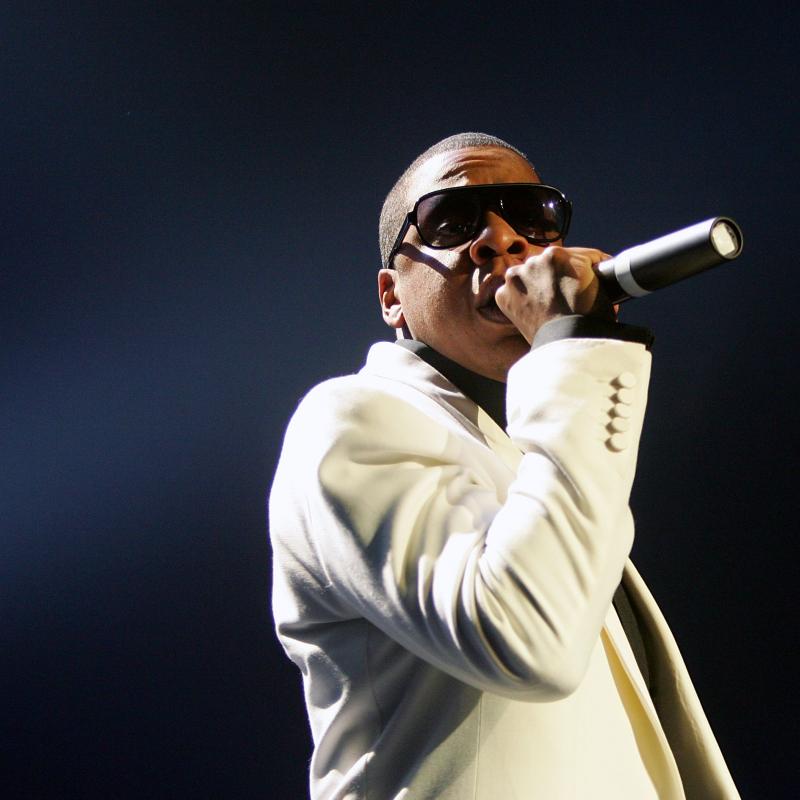 Rapper Jay-Z holding a mic and performing on stage in a white suit