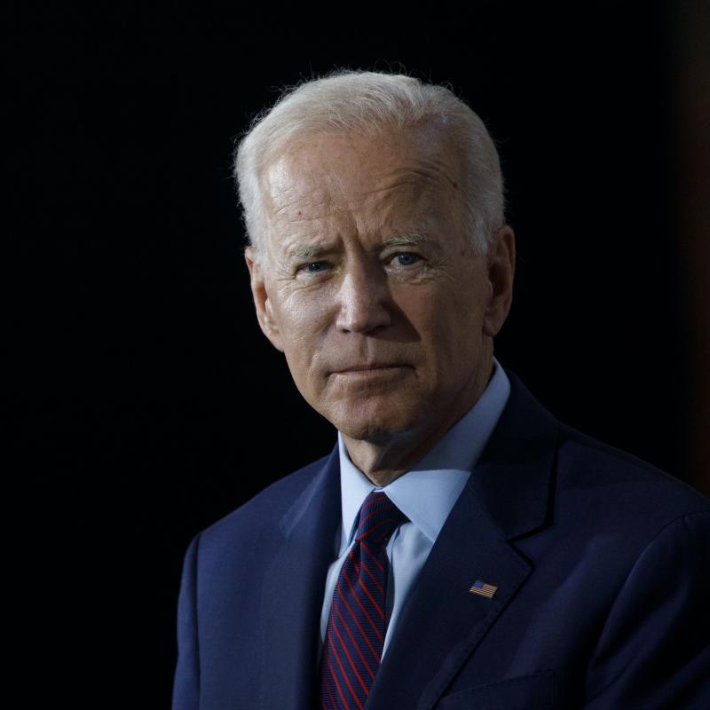 Joe Biden looks away from the camera in a dark suit against a black background