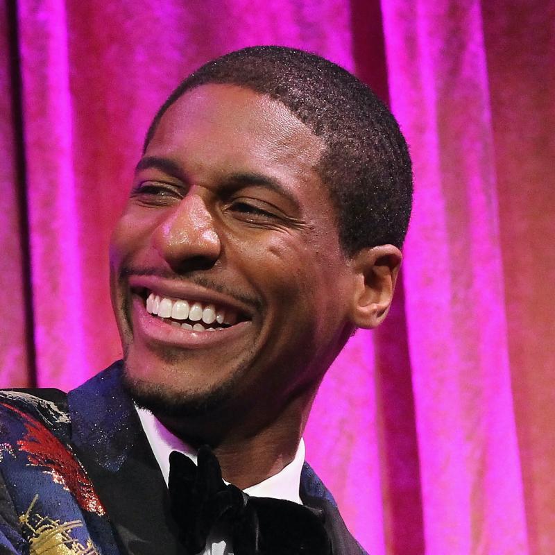 Musician Jon Batiste smiles while playing the piano