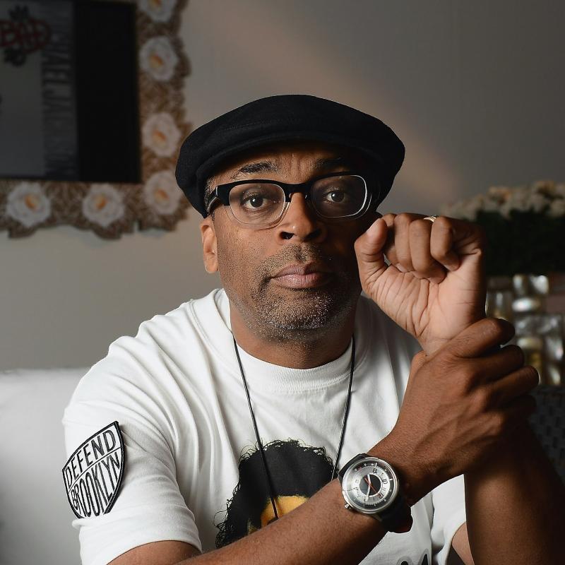 Film director Spike Lee raises his fist in a pose for a seated portrait